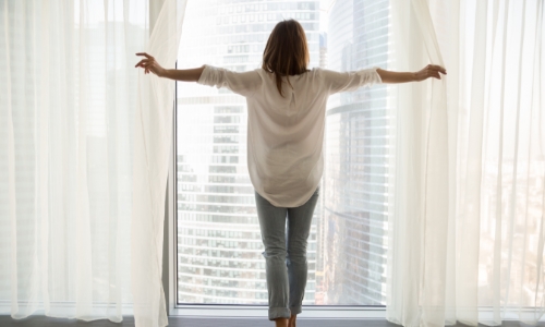 A person standing in a large picture window looking out