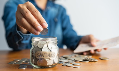 A woman's hand putting coins in a jar.