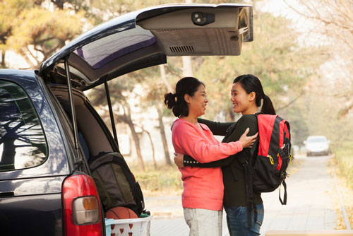 A mother and daughter are hugging each other at the back of their car