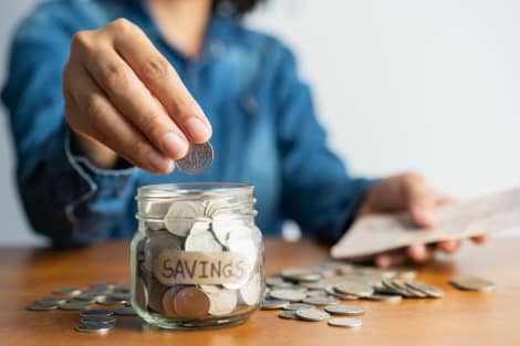 A woman putting coins into a jar marked savings