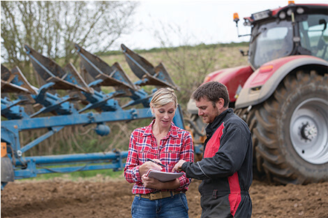 two farm employees with a tractor behind them